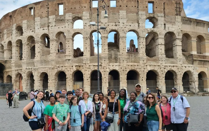 Group of students and adults pose in front of the Colosseum in Rome during a field trip.
