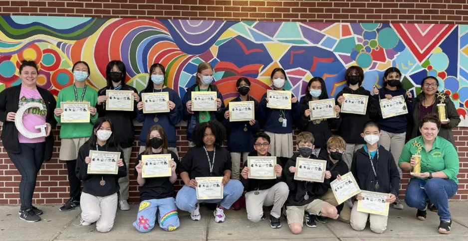 Group of students holding certificates and medals in front of a colorful mural with staff.