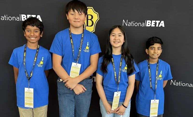 Four students in matching blue shirts and lanyards pose in front of a National Beta backdrop.