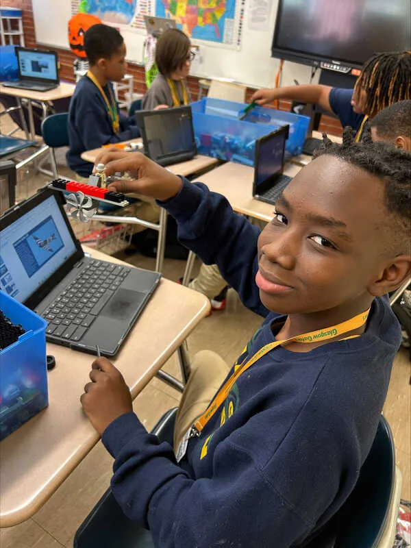 Student holding a small LEGO build next to a laptop.