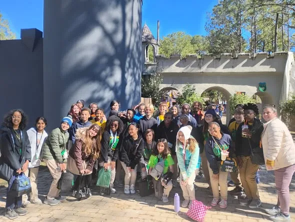 Group of students posing together outdoors near a castle-style structure on a sunny day.