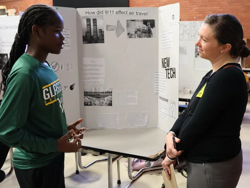 Student presenting a project on how 9/11 affected air travel to an adult evaluator.