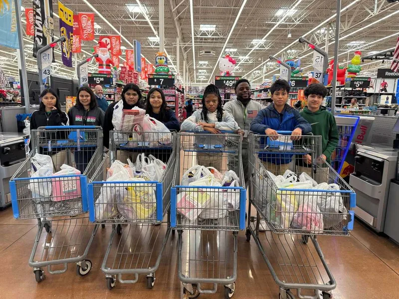 Group of students with full shopping carts standing in a store checkout area with holiday decorations.
