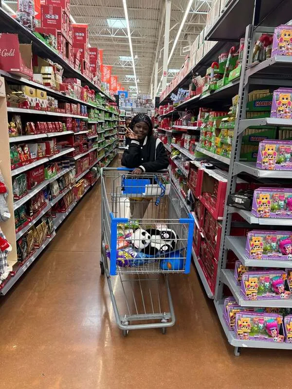 Person leaning on a shopping cart in a store aisle with holiday candy and toys on shelves.

