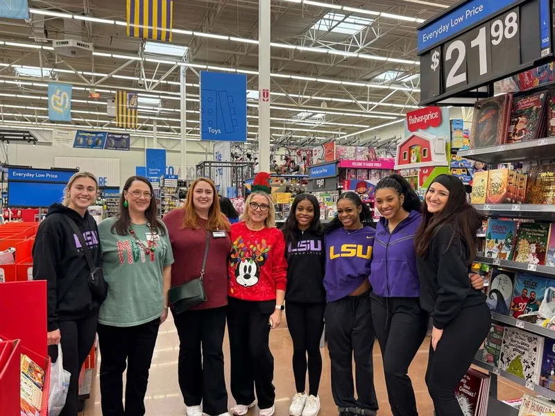 Group of adults and students pose in a store toy aisle under “Everyday Low Price $21.98” sign.