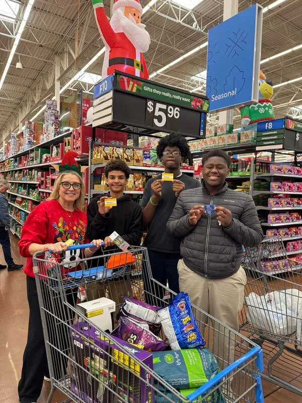 Four people with shopping carts full of items holding receipts in a store aisle under holiday decor.


