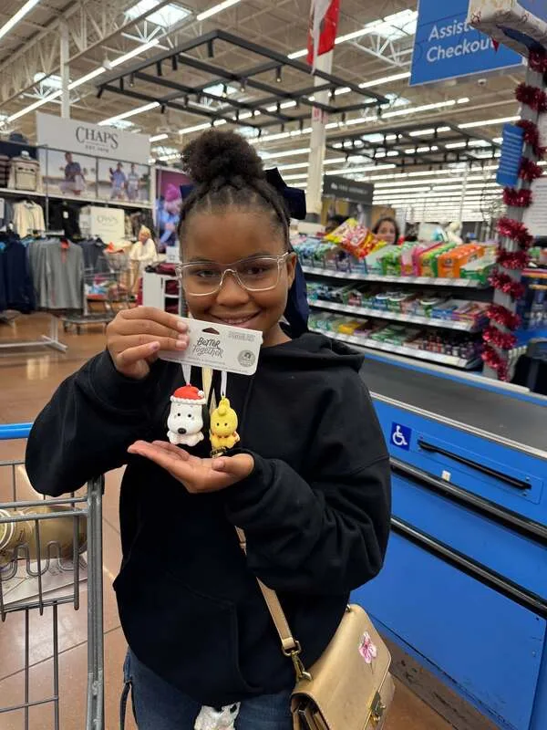Child holding small toys and a receipt near a checkout area in a retail store.
