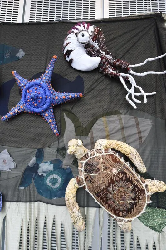 Textile sea creatures--jellyfish, starfish, and turtle--displayed on a dark backdrop wall.