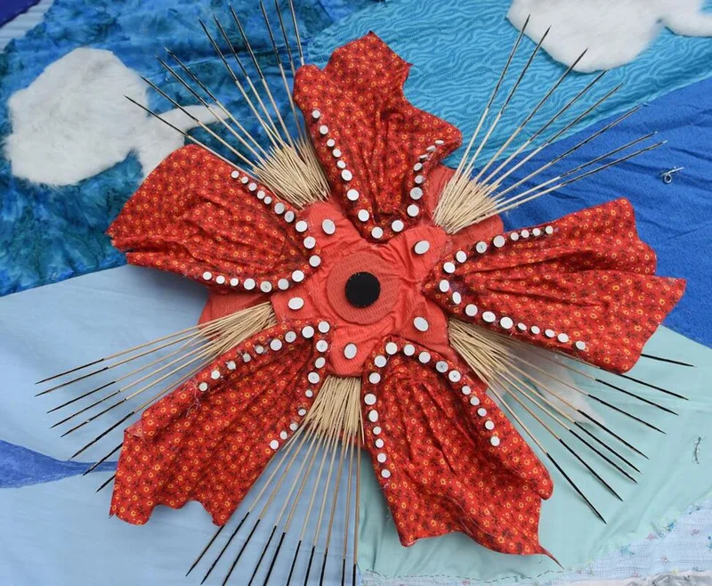Red flower-like sculpture made of fabric and sticks with radial design on a blue background.