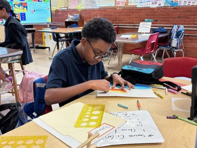 Student uses a ruler and stencil to measure and draw shapes during a classroom activity.