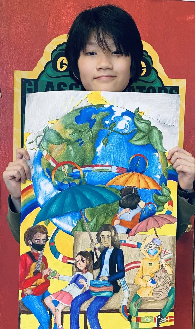 Student holds a colorful drawing of Earth, people, and peace symbols in front of a red wall.