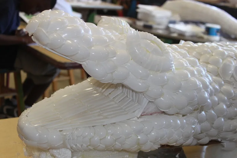 White alligator sculpture resembling layered scales or petals made from cafeteria sporks. 