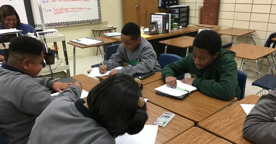 Four students sitting in desks that are arranged in a group. They are working on an assignment. 