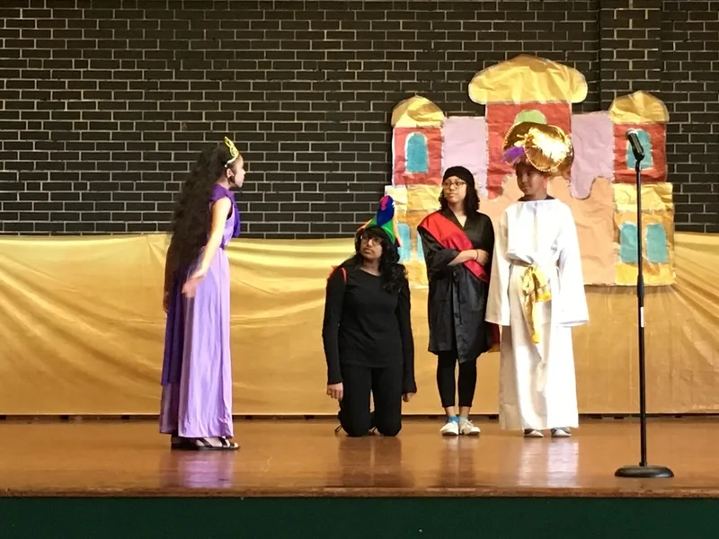 A girl dressed as a princess speaks with three students. 