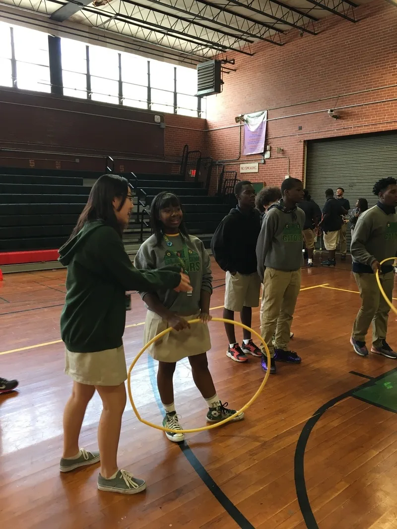 Two female students standing in the gym with a hula hoop