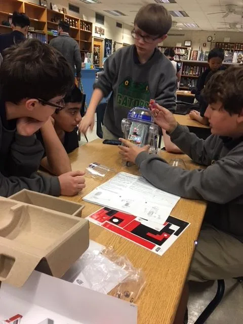 Three male students seated a table. They are building a robot. 