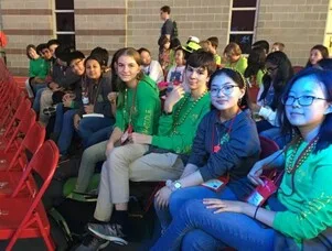 Students seated in red chairs at an event, wearing medals and lanyards, gathered in a group.