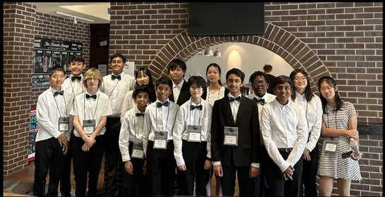 Group of students in formal attire with bow ties posing together in front of a brick archway.