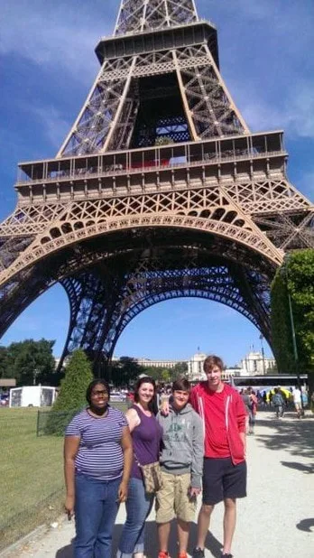Students/teachers pose in front of the Eiffel Tower in Paris on a sunny day.
