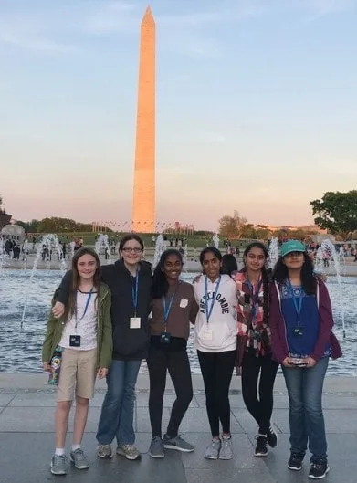 Six students stand in front of the Washington Monument and fountain at sunset.
