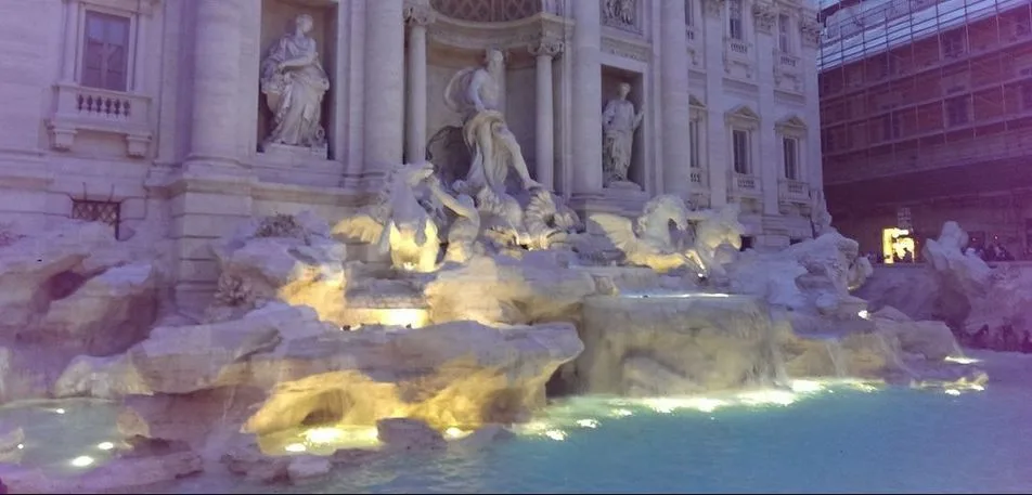 Trevi Fountain in Rome lit at dusk, with statues and flowing water in a stone plaza.